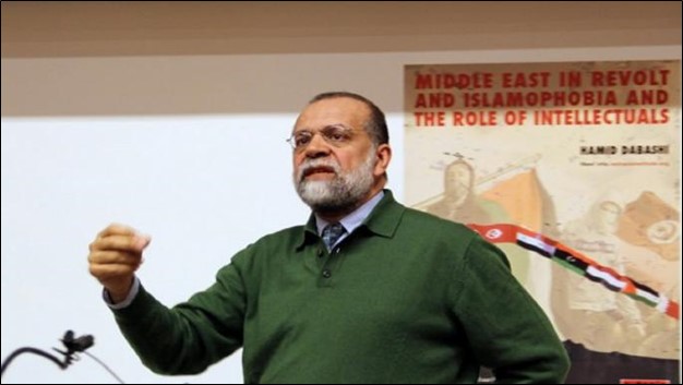 An image of Hamid Dabashi standing at a podium