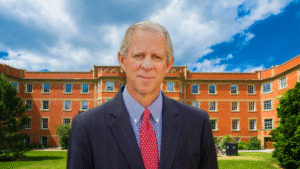 University of Arizona President Robert Robbins stands in front of a red-brick campus building under a partly cloudy sky, symbolizing university leadership amid rising campus tensions over Israel-Hamas protests.