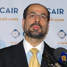 Nihad Awad, co-founder and executive leader of CAIR, speaking at a public event, wearing a suit and tie and standing at a podium.